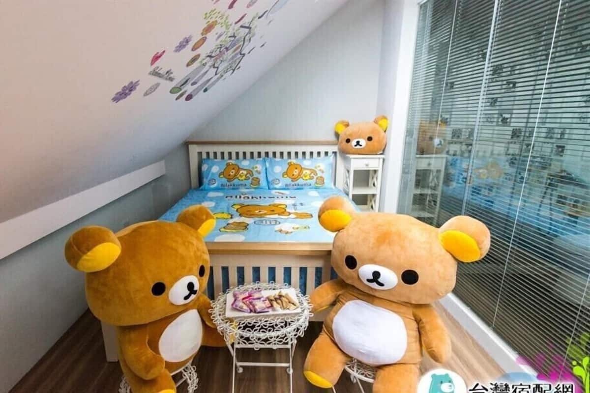 A bedroom with a bed featuring a bear-themed duvet cover, two teddy bears on either side of the bed, and a small table with snacks.