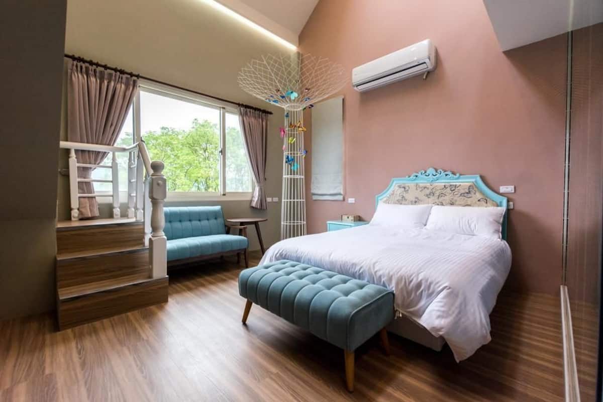 A bedroom with a bed, a blue chair, a wooden staircase, and a window with curtains.