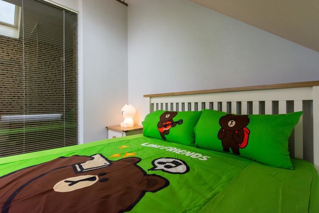 A bedroom with a green bedspread featuring bear designs, a white headboard, and a window with blinds.