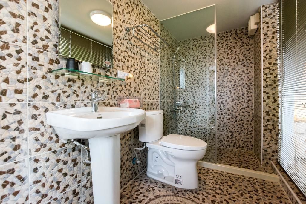 Un baño con pared de mosaicos, un estante de vidrio con artículos de aseo, un lavamanos blanco y un inodoro.
