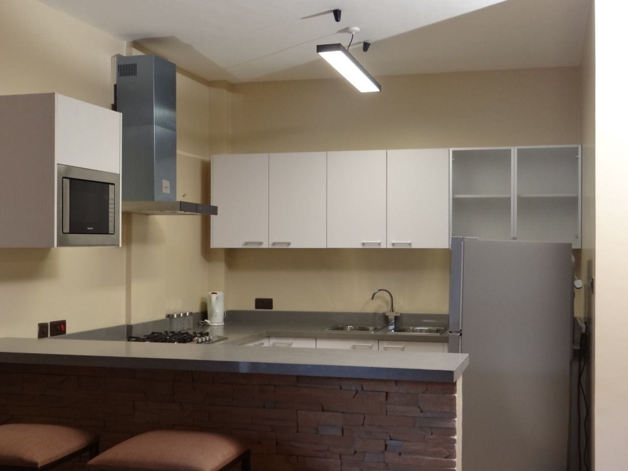 A kitchen with a built-in stove, a sink, and a refrigerator. There are cabinets above the counter and a ceiling fan.