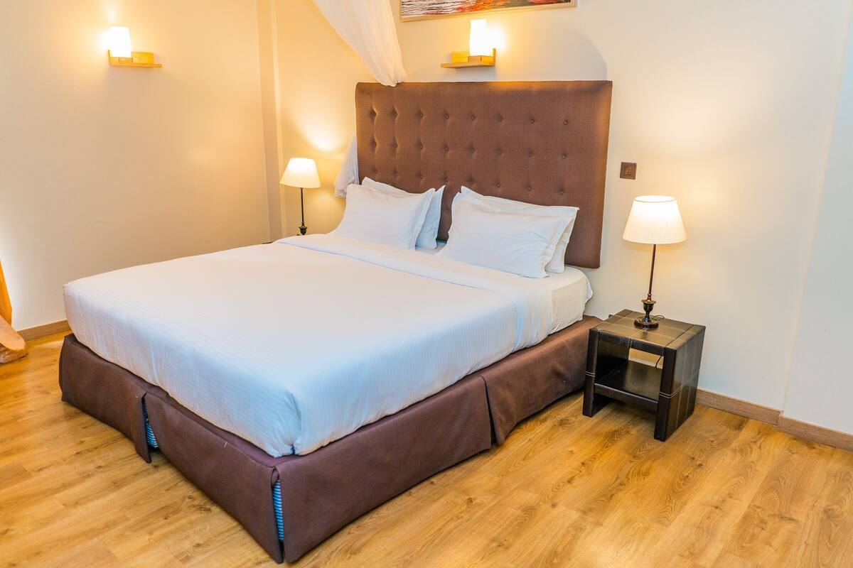 A neatly made bed with a brown headboard, two bedside lamps, and a wooden floor.