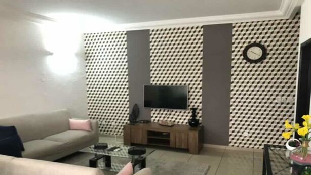 A living room with a sofa, a coffee table, a TV on a wooden stand, and a patterned wall.