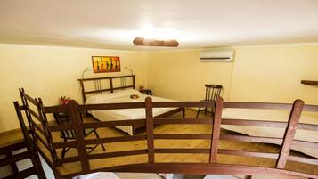 Una habitación pequeña y acogedora con una cama individual, una silla de madera, una mesita y aire acondicionado instalado en la pared.