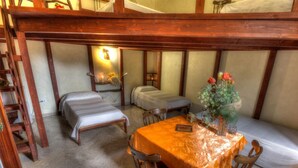 Um quarto aconchegante com duas camas de solteiro, uma mesa de madeira com um vaso de flores e uma escada encostada na parede.