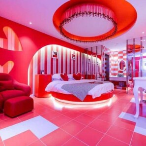 Un dormitorio moderno con una lámpara de techo circular, una cama con ropa de cama roja y blanca, y un sillón rojo.