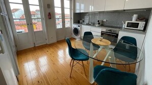A compact kitchen with a glass dining table, teal chairs, and a washing machine. - Mezzanine Apartment in the heart of Guimarães. (Guimarães)