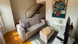 A modern living room with a sofa, ottoman, and a flat-screen TV. - Mezzanine Apartment in the heart of Guimarães. (Guimarães)