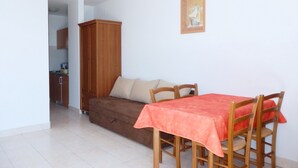 A small room with a sofa, a dining table with four chairs, a wooden cabinet, and a painting on the wall. - Apartments Idila (Medulin)