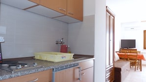 A kitchen with wooden cabinets, a granite countertop, a stove, and a dining area with a table and chairs. - Apartments Idila (Medulin)