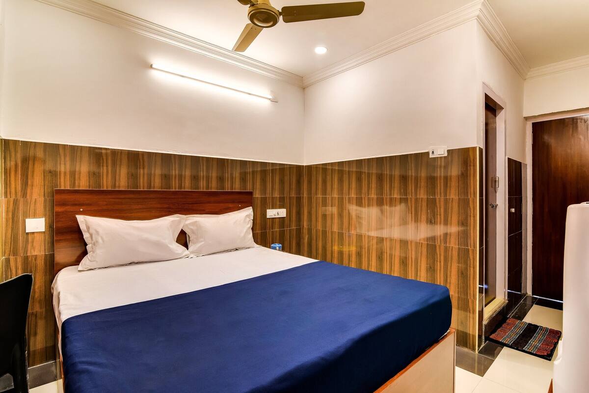 A hotel room with a bed, a ceiling fan, and a shower area.