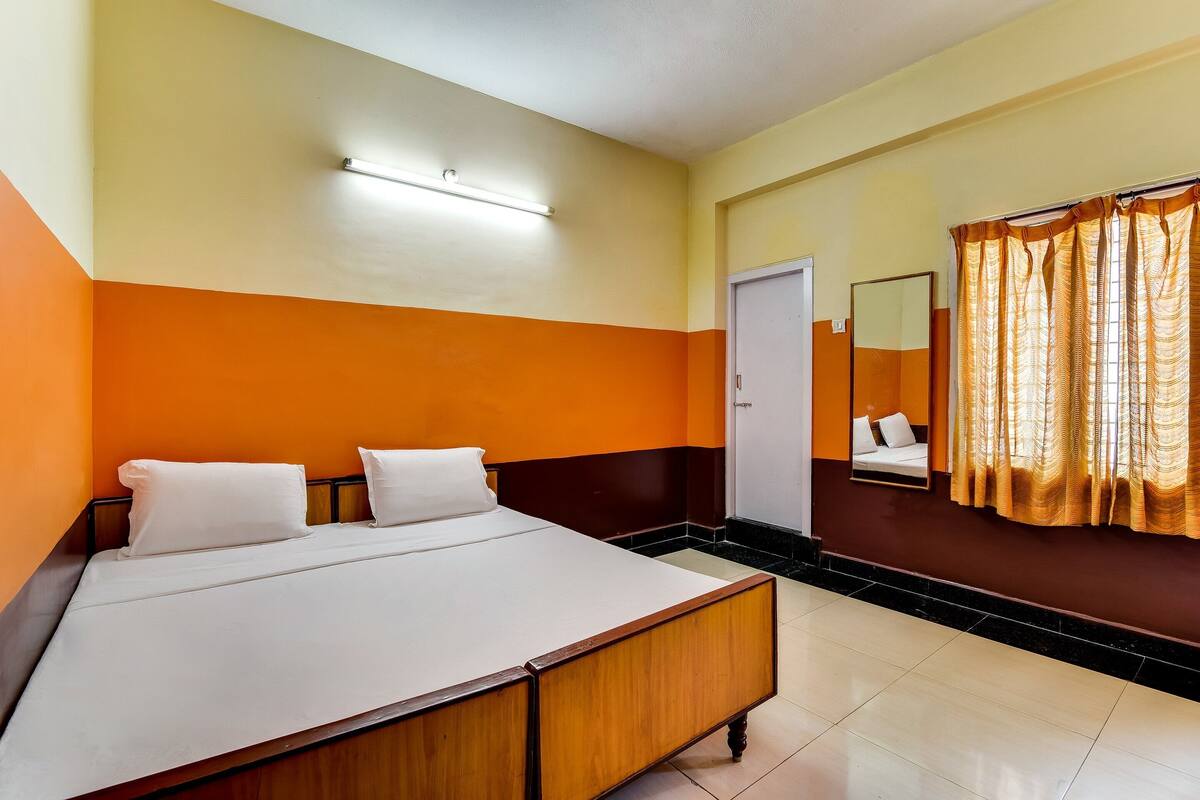 A hotel room with a bed, a mirror, and a window with curtains.