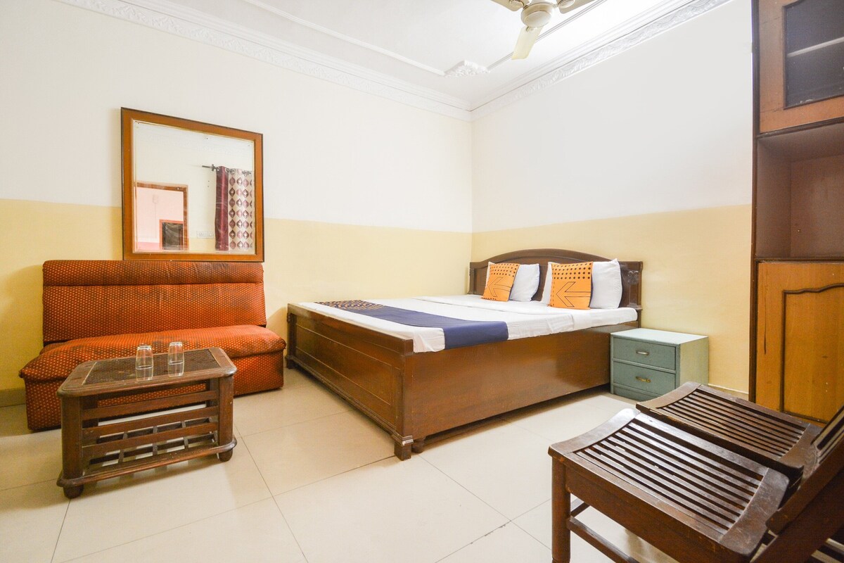 A bedroom with a bed, a wooden nightstand, a small table, a chair, and a sofa.