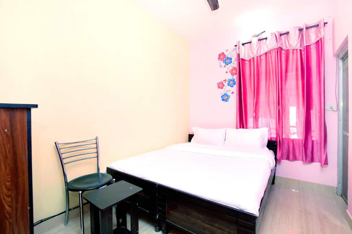 A bedroom with a bed, a chair, a small table, and a wall decoration.