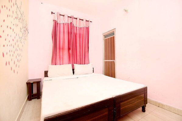 A bedroom with a wooden bed, pink curtains, a small bedside table, and a window with a wooden blind. - SPOT ON 37127 Primeland (Mohali)