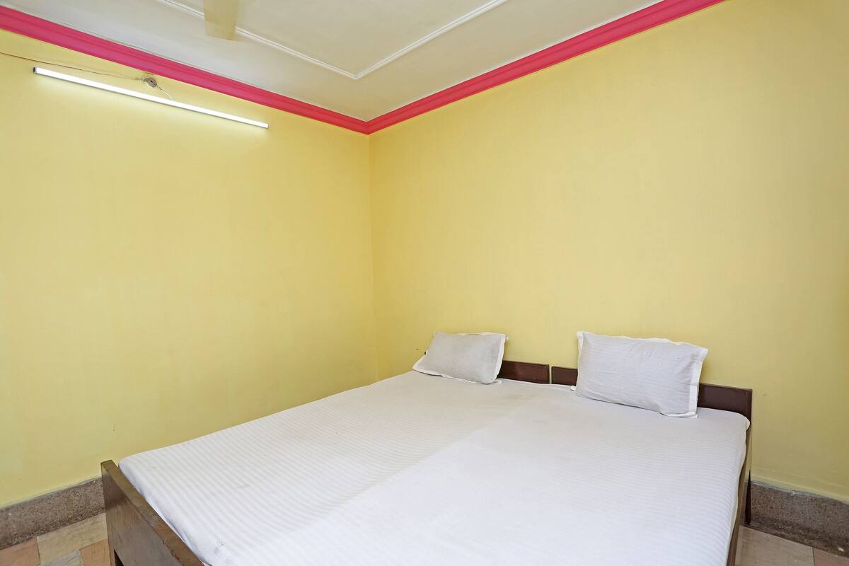 Quarto com cama, duas almofadas e luminária no teto.