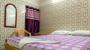 Una habitación de hotel con cama, sillón, mesita de noche, espejo y papel tapiz estampado.