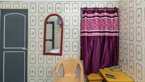 Una habitación con puerta, espejo, silla, mesa, teléfono y cortina.
