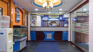 Un área de recepción con una paleta de colores azul y marrón, un candelabro, una mesa de recepción y un dispensador de agua.