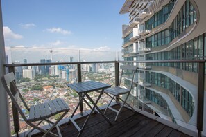 A balcony with a table and chairs, overlooking a cityscape with modern buildings and a tower. - OHO Suites KLCC Setia Sky (Kuala Lumpur)