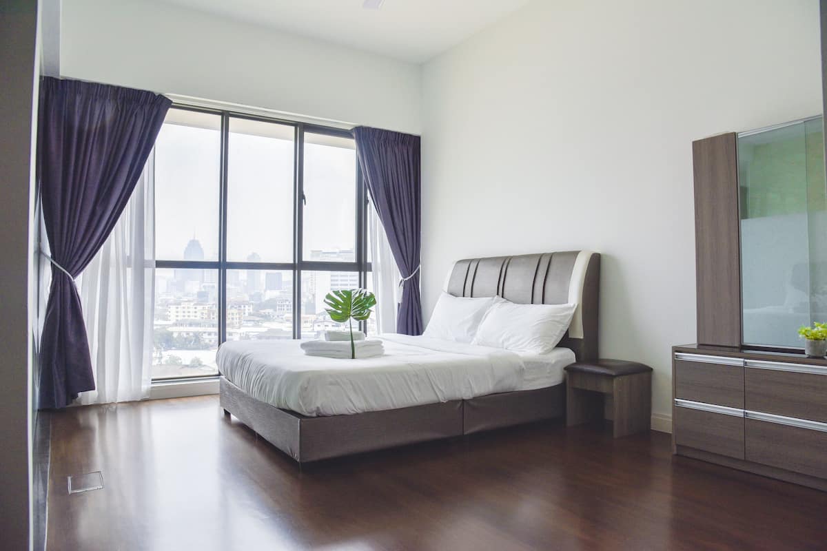 A modern bedroom with a large window, a bed, a nightstand, and a dresser.