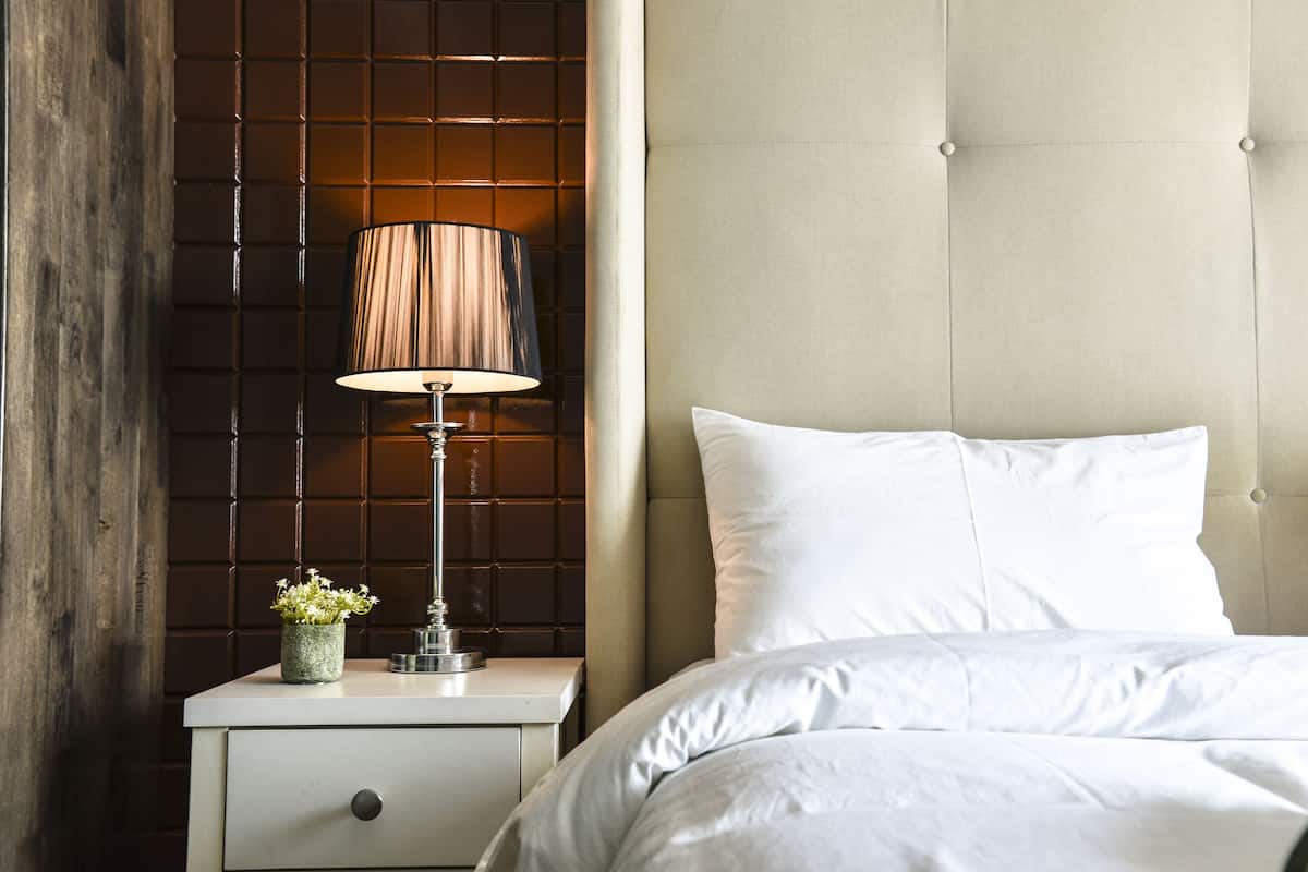 A neatly made bed with white linens, a bedside lamp, and a small potted plant on a nightstand.