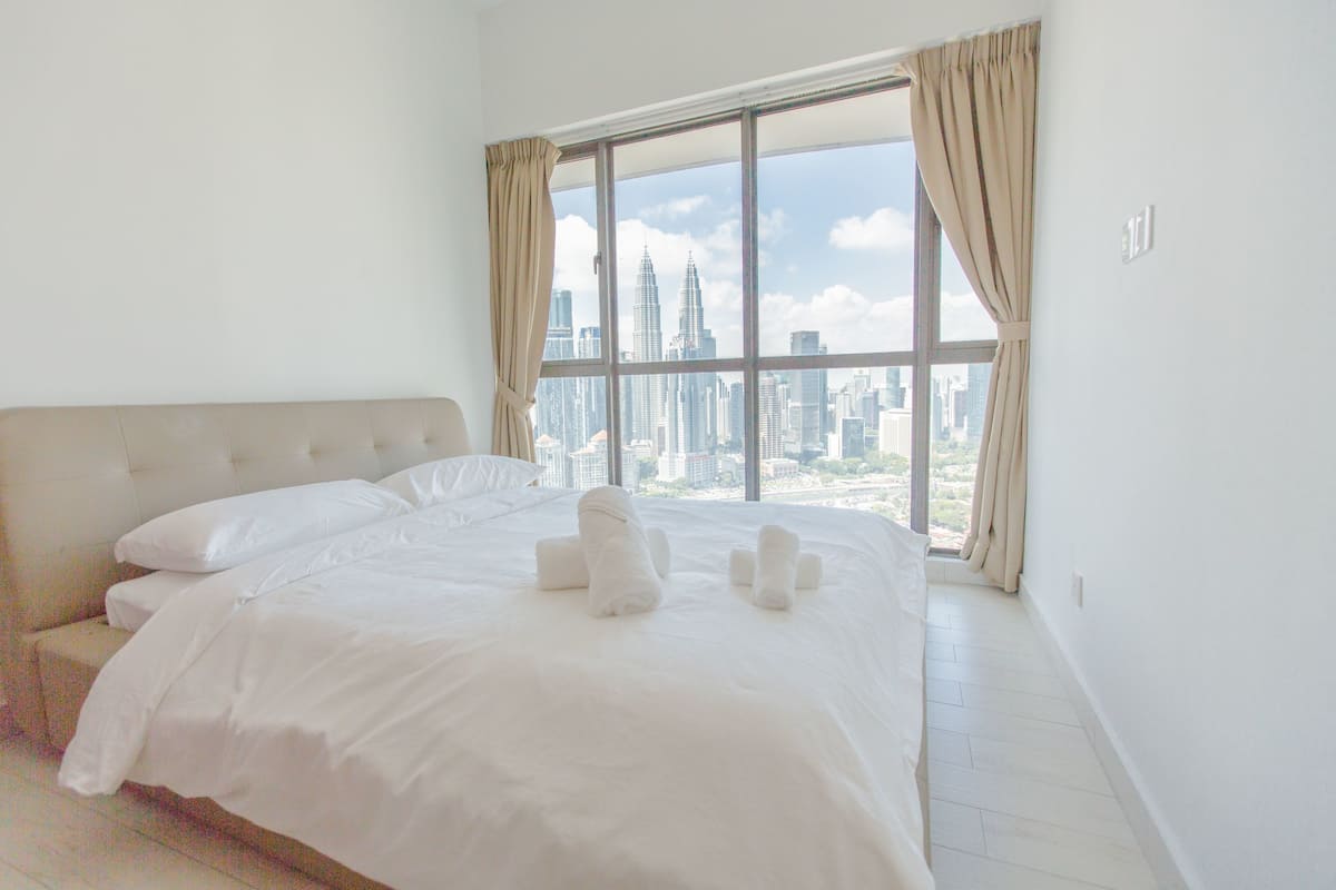 A hotel room with a large bed, a view of a cityscape through a window, and a city skyline visible outside.