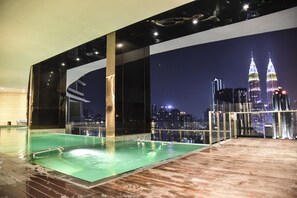 An indoor swimming pool with a cityscape view, including the Petronas Towers, and a wooden deck area. - OHO Suites KLCC Setia Sky (Kuala Lumpur)