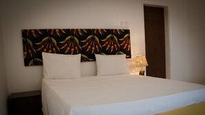 Una cama con ropa blanca, un cabecero de estampado colorido y una lámpara de noche.