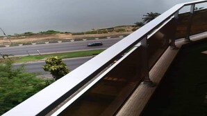 A view from a balcony overlooking a road with a body of water in the background. - Résidence Djény T3 (Abidjan)
