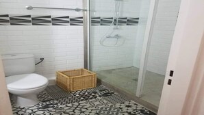 A bathroom with a toilet, a shower with glass doors, and patterned floor tiles. - Résidence Djény T3 (Abidjan)