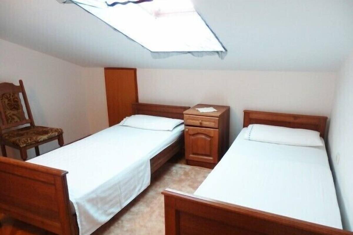 Um quarto pequeno e simples com duas camas de madeira, uma cadeira e um armário de madeira.