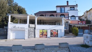 A restaurant with a white facade and a covered outdoor seating area. - Apartments La Playa (Medulin)