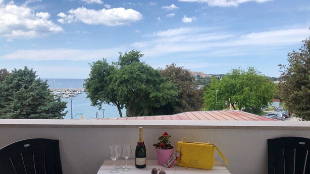 A balcony with a table set for two, a bottle of champagne, glasses, a potted plant, and a yellow bag. - Apartments La Playa (Medulin)