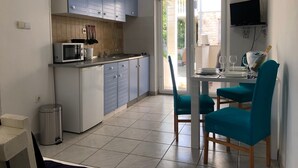 A compact kitchen with a microwave, sink, and blue cabinets. There is a dining area with teal chairs and a table, and a TV mounted on the wall. - Apartments La Playa (Medulin)