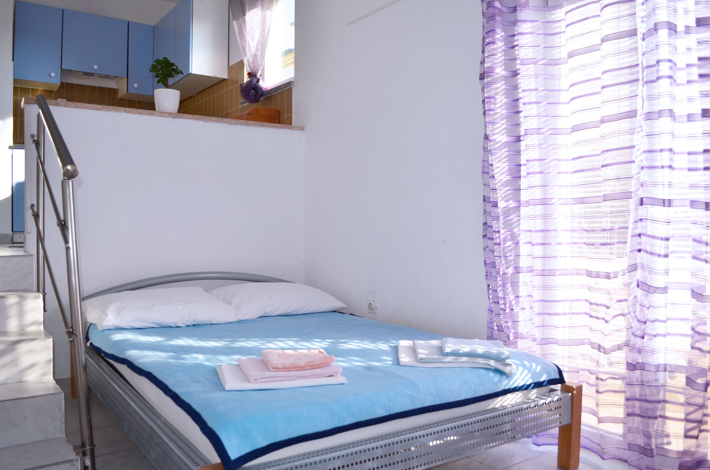 Ein Schlafzimmer mit einem Bett, einem Fenster mit Vorhängen, einer Treppe und einem Blumentopf.