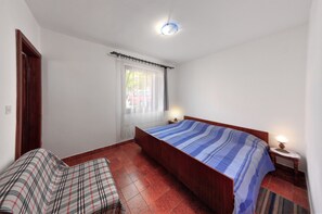 A bedroom with a bed, a nightstand, a lamp, a window with curtains, a door, and a small sofa. - Vesna (Medulin)