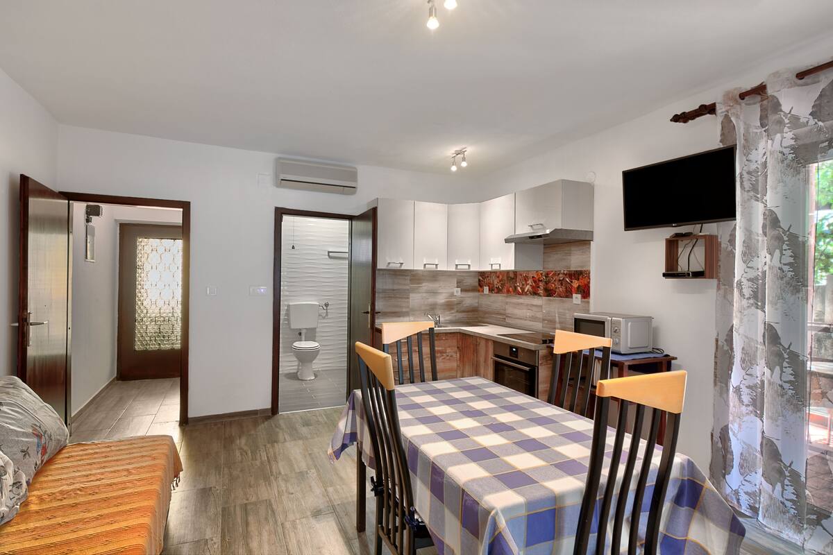 A compact kitchen with a microwave, stove, and sink. There is a dining table with chairs and a TV mounted on the wall.