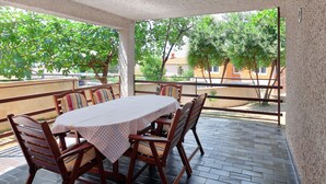 Une terrasse extérieure avec une table et des chaises, une vue sur les arbres et les bâtiments, et une rambarde en métal.