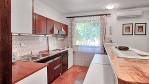 Une cuisine compacte avec des meubles en bois, un évier à deux bacs et une fenêtre donnant sur un espace verdoyant.