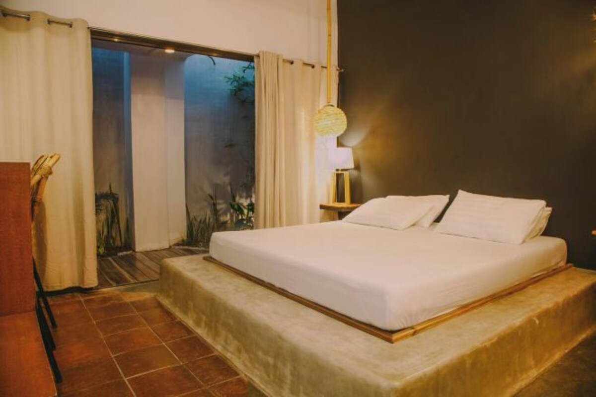 Une chambre à coucher avec un lit, des rideaux, une table de chevet et une lampe.