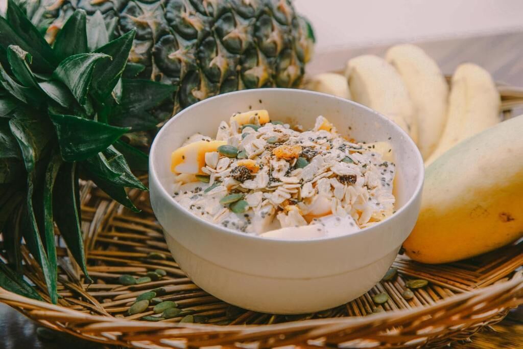 A bowl of food with a pineapple and bananas in the background.