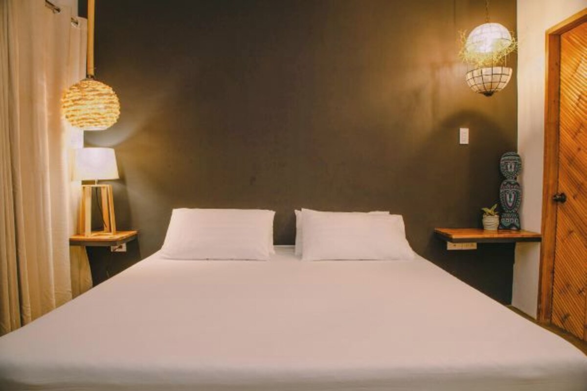 Un lit bien fait, avec du linge de lit blanc, deux tables de chevet avec des lampes et une porte en bois.