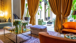 A modern living room with a sofa, ottoman, coffee table, and a dining area with a tray of snacks. - Riad Tajania (Marrakech)