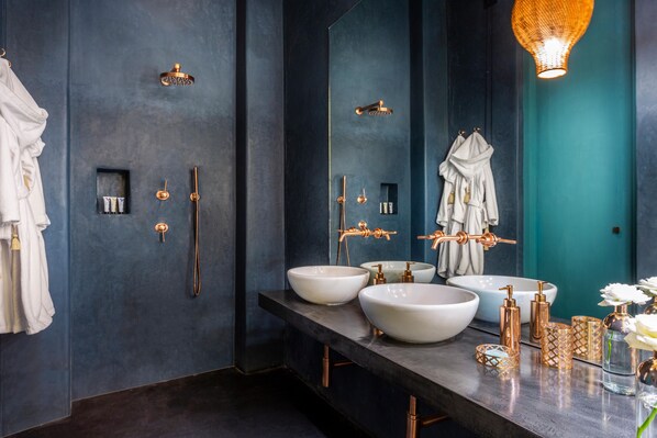 A modern bathroom with dark walls, two large white sinks, gold fixtures, and a mirror reflecting a robe.
