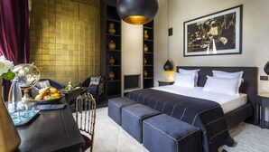 A modern hotel room with a large bed, a seating area, a dining table, and a bookshelf. - Riad Tajania (Marrakech)
