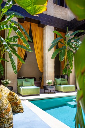 A poolside area with a seating arrangement, a pool, and tropical plants.