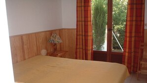 A bedroom with a bed, a nightstand, a lamp, and a window with curtains. - T2 MEZZANINE + TERRACE SAINT CYPRIEN BEACH (Saint-Cyprien Plage)