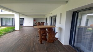A modern outdoor area with a wooden table and chairs, a covered patio, and a view of a building in the background. - Résidence Akwaba T7 (Abidjan)