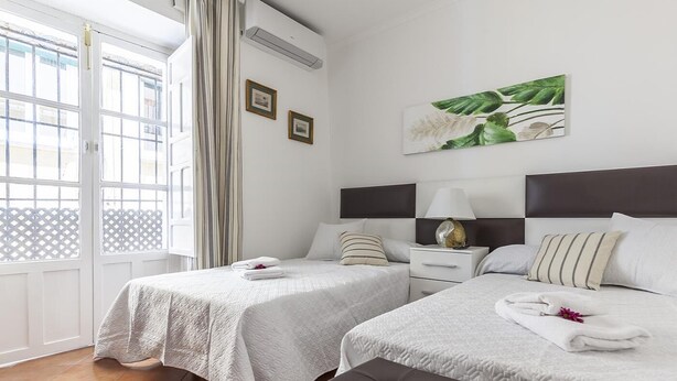 Une chambre d’hôtel avec deux lits, une grande fenêtre avec des rideaux, un climatiseur fixé au mur et un tableau encadré.